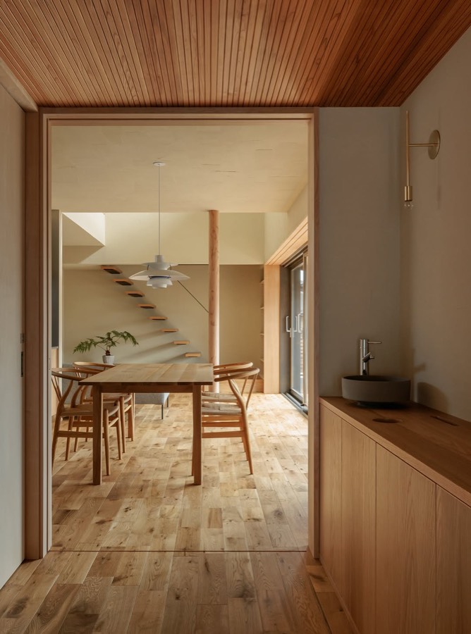 A timber-lined room with a dining table, seen through an opening with a staircase beyond.