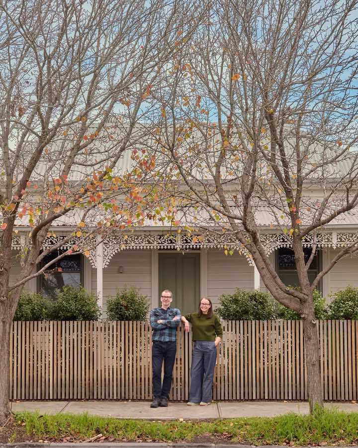 Two people standing at the timber picket fence of a Victorian cottage with iron lacework.