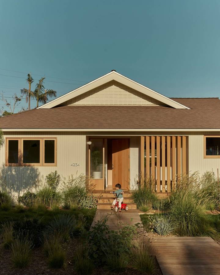 A cream painted bungalow with a slatted timber porch screen, with native planting and a timber path in front.