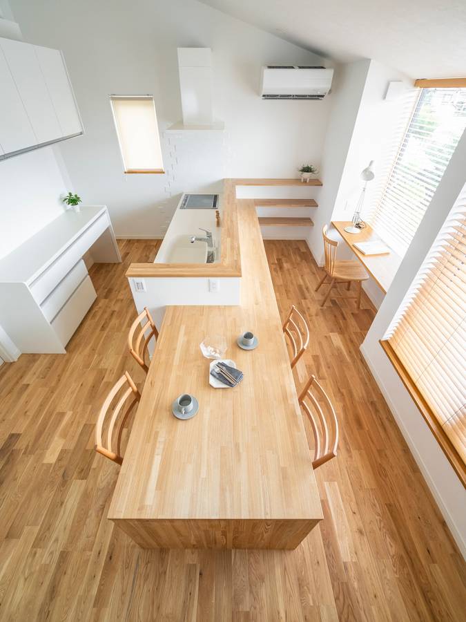 A pale timber dining table and a built-in study counter in a white room with a sloping ceiling.