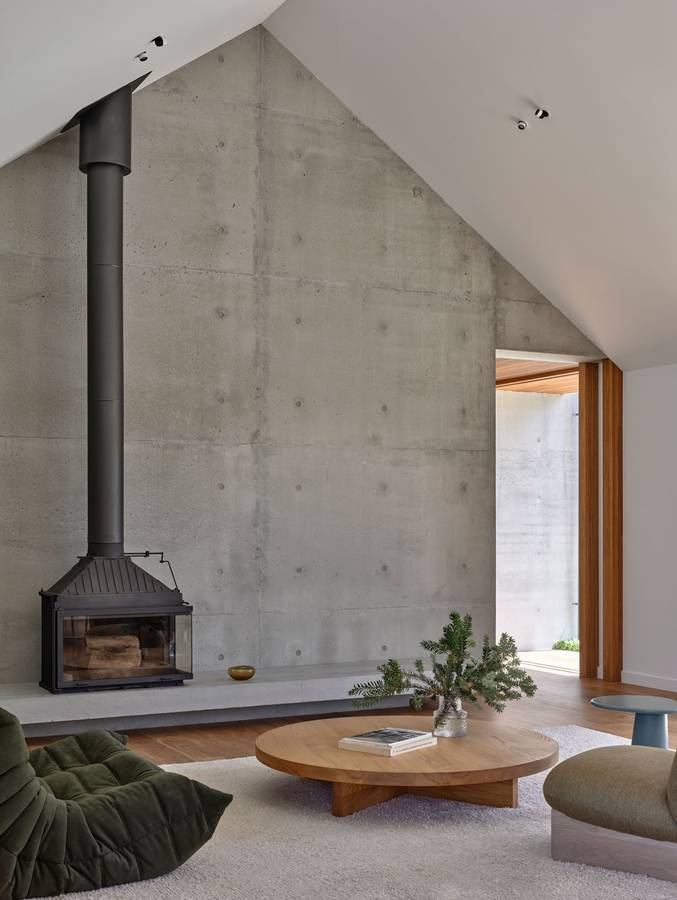 A living room with a board formed concrete wall, a black wood heater and a white raked ceiling.