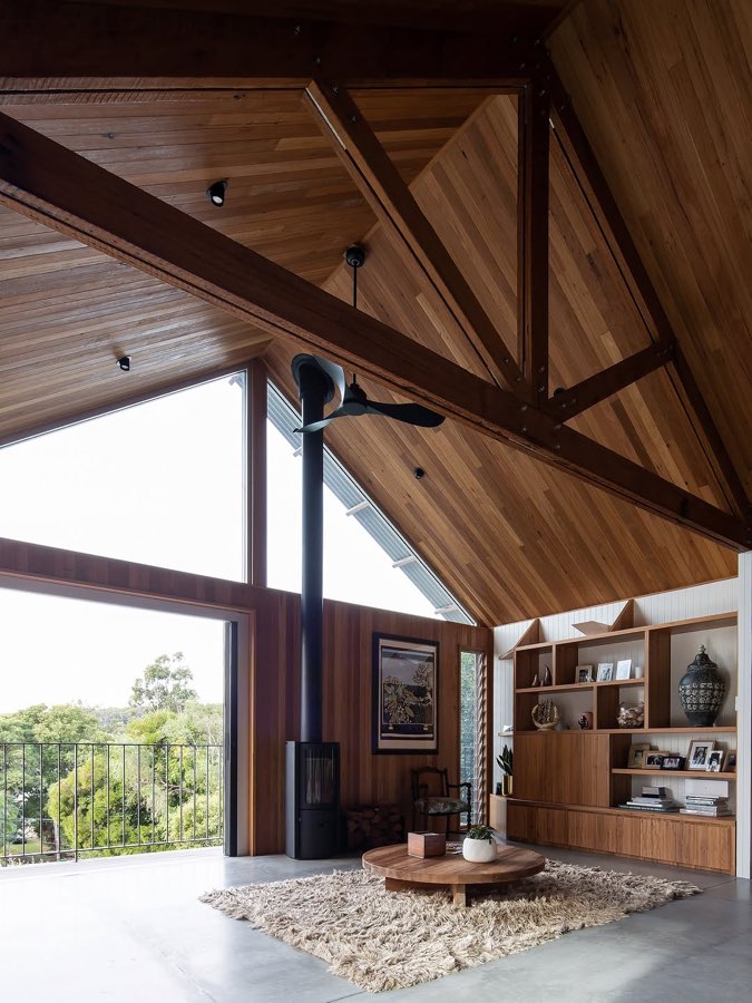 A timber cathedral ceiling with exposed trusses above a living room with a wood fire and full-height glass.