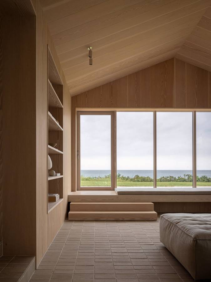 A timber lined gabled room with built-in shelves and a window seat looking out to the sea.