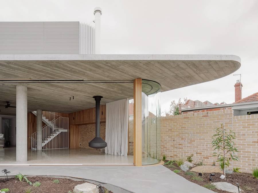 A curved concrete roof cantilevering over a timber lined room with a suspended black fireplace.