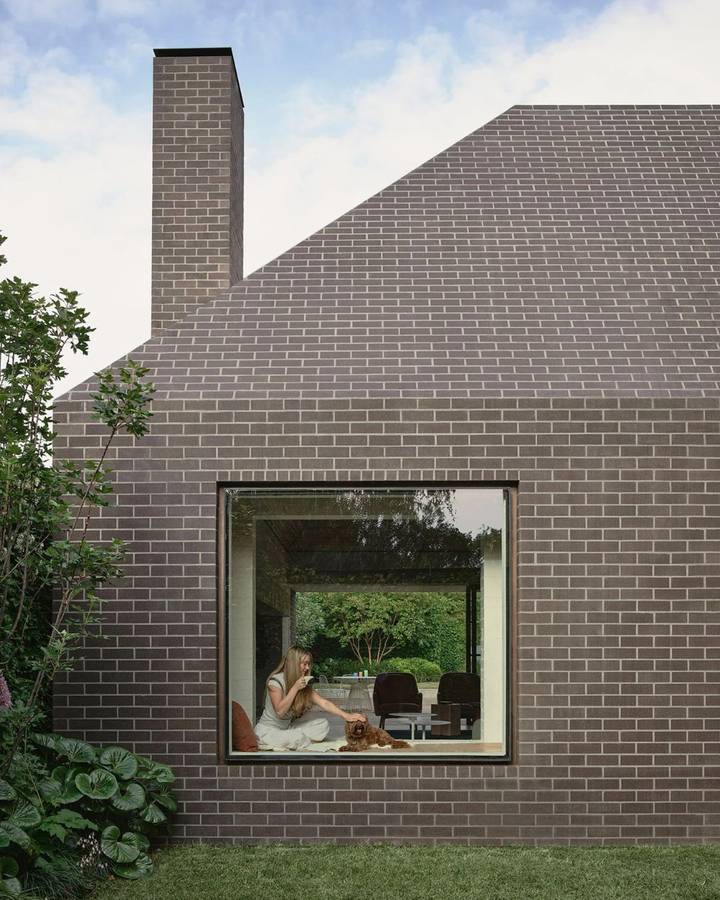A brick gable wall with a tall chimney and a single large square window with a window seat inside.