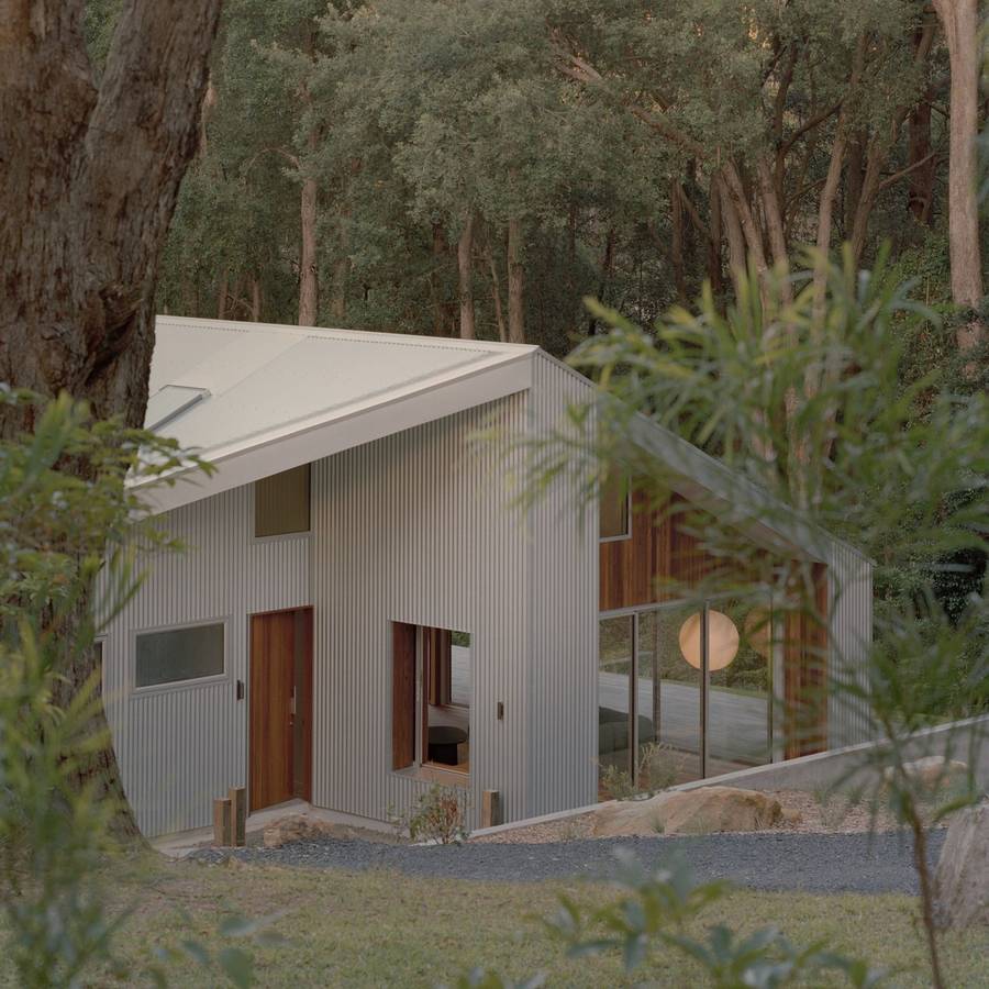 A corrugated metal clad house with a skillion roof standing among gum trees on a gravel apron.