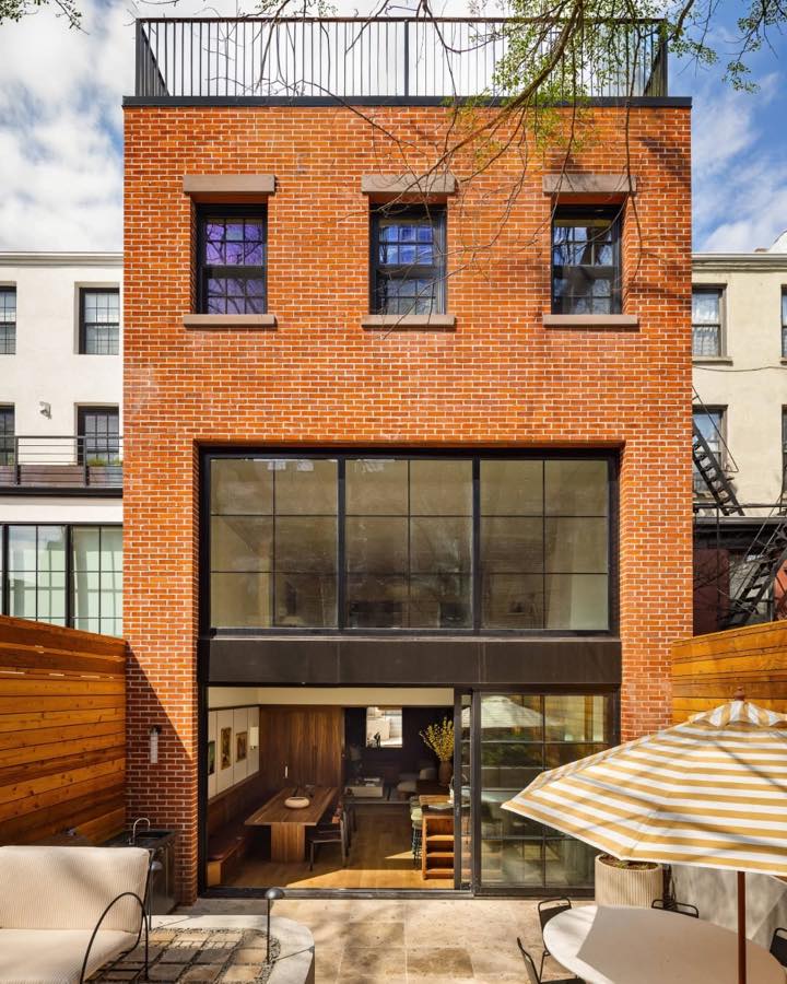 The rear of a red brick townhouse with a fully glazed garden level and a striped umbrella in the garden.