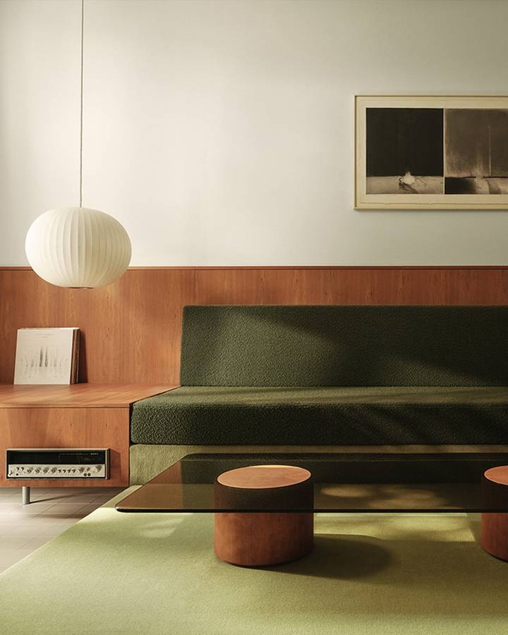 A living room with a timber panelled dado, a built in green sofa, a green carpet and a white paper pendant.