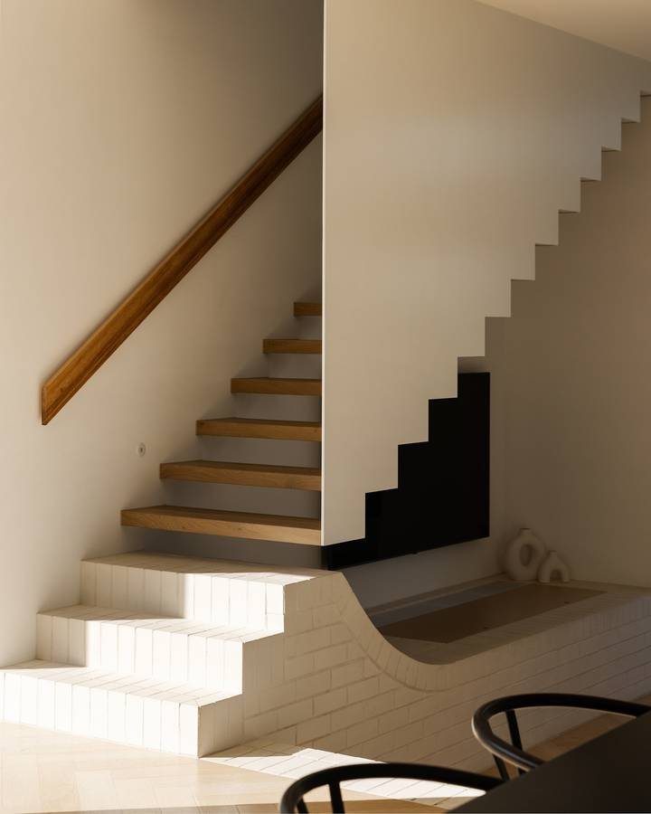 A stair with pale timber treads against a rendered wall, above a lower run of white tiled steps.