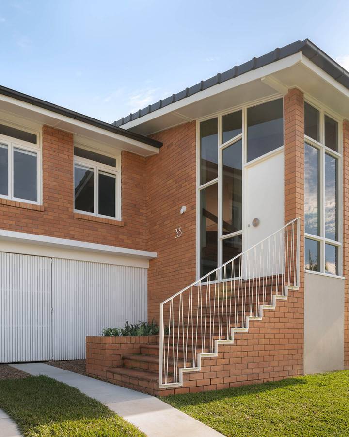 A brick mid century house with a white steel stair up to the front door and a garage below.
