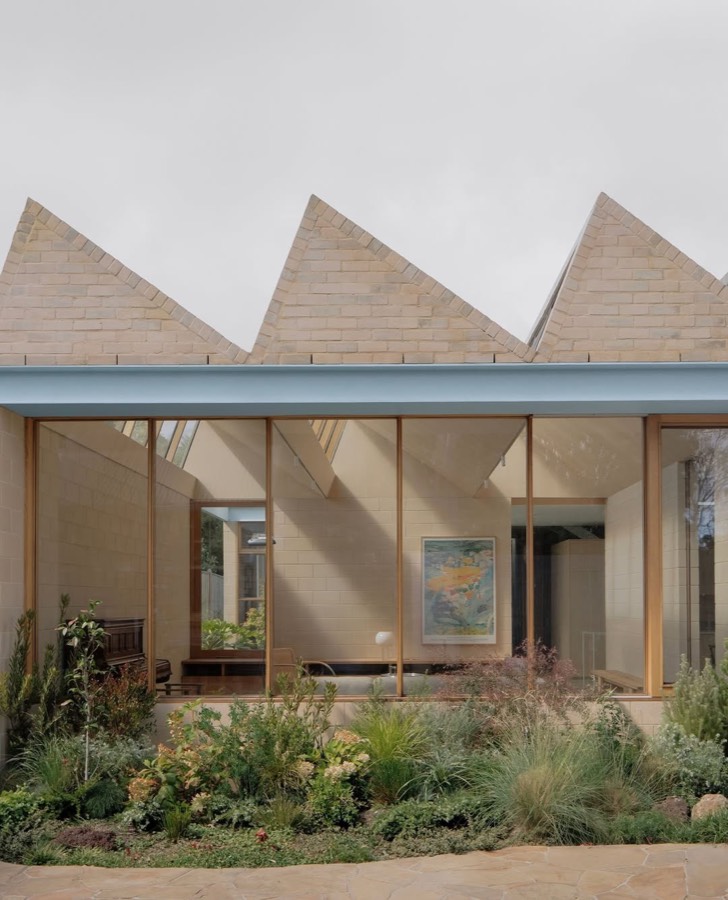 A house with three steep gabled roof forms above a glazed front, with a planted garden in front.