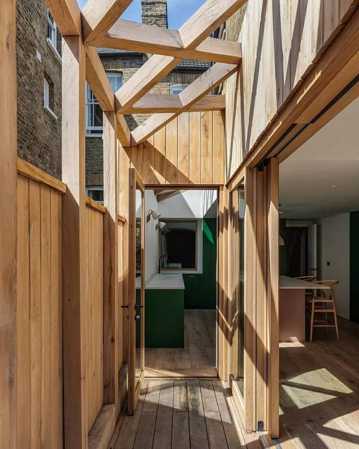 A narrow oak framed side passage with exposed rafters and sliding doors, seen along a timber deck beside a brick party wall.
