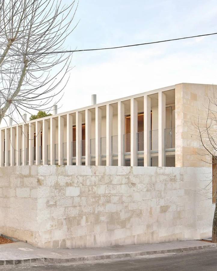 A pale stone building with a row of slender vertical fins above a sandstone wall, seen from a street corner.