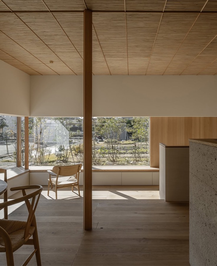 A room with a woven reed ceiling and a timber post, with low windows looking onto a garden.