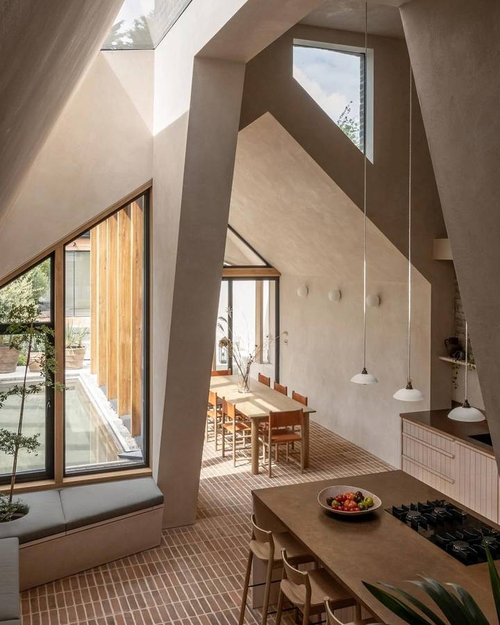 A double height kitchen and dining room with clay plastered walls cut by skylights, oak joinery and a long dining table on a tiled floor.