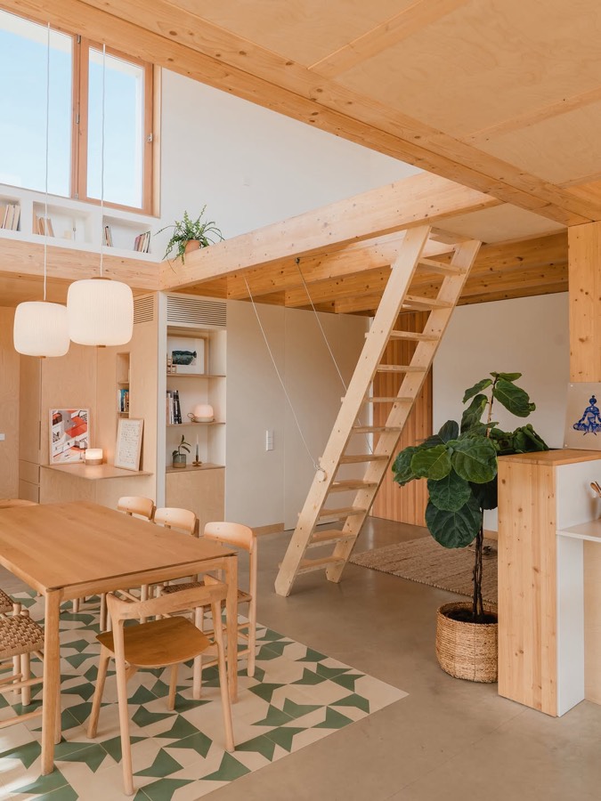 A timber lined room with a ladder up to a loft, a dining table and a patterned green tile floor.