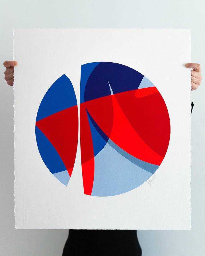 A person holding a large sheet of cotton paper painted with a circle split into blue and red curved forms.