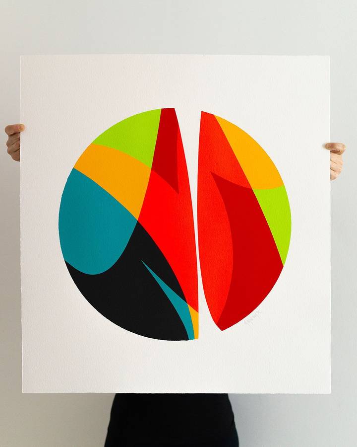 A person holding a large sheet of paper painted with a circle split into green, orange, red, teal and black forms.
