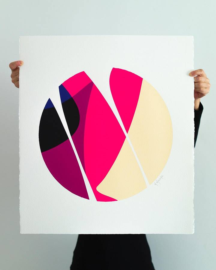 A person holding a large sheet of paper painted with a circle split into pink, magenta, cream and black forms.