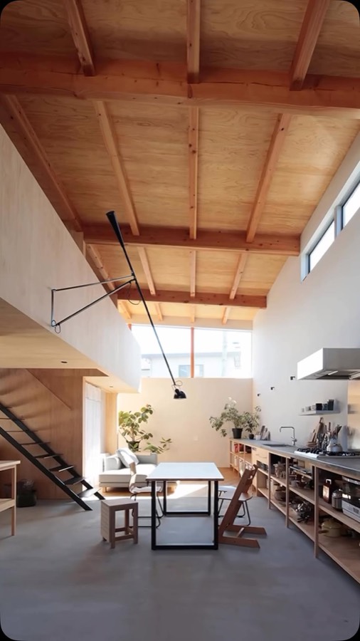 A double height room with an exposed timber roof structure, a dining table and a steel stair.