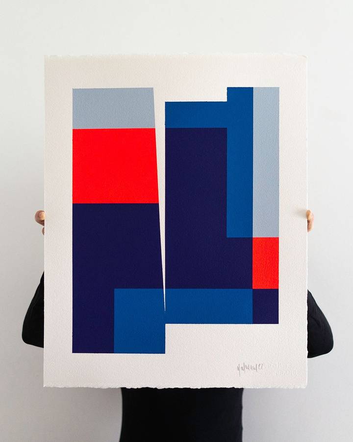 A person holding a sheet of paper painted with navy, blue, red and grey interlocking blocks.
