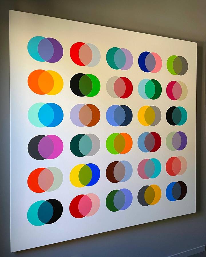 A large square canvas on a wall painted with a grid of overlapping translucent circles in many colours.