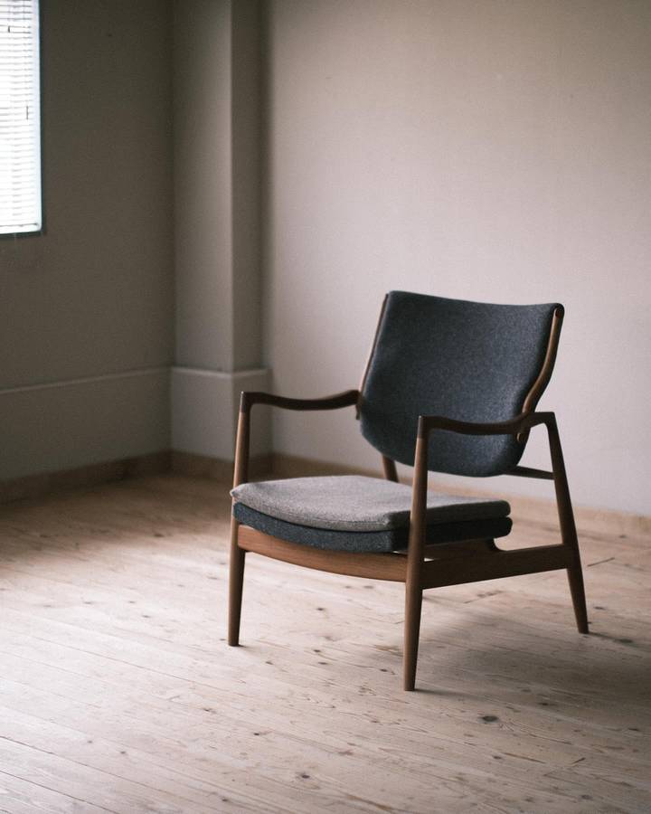 A timber framed easy chair with a charcoal upholstered back and a pale grey seat cushion, standing on floorboards in an empty room.