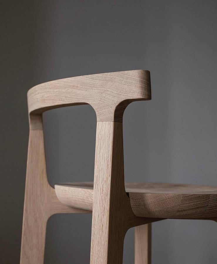 A close view of a pale oak chair where the curved backrest meets the leg, with the seat behind.
