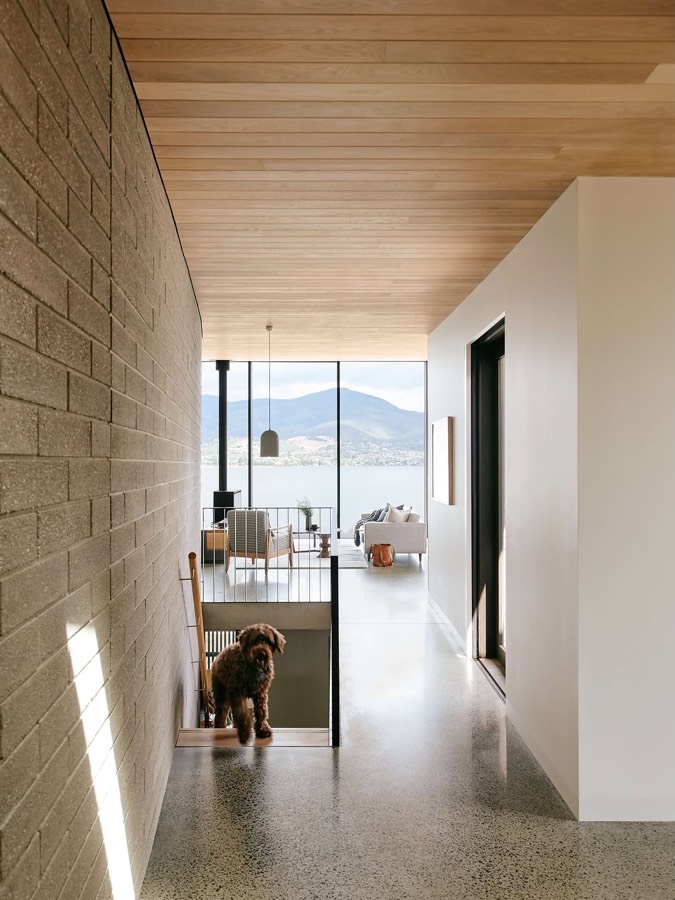 A corridor with a concrete block wall on one side and a timber ceiling, looking through to a room with a mountain view.