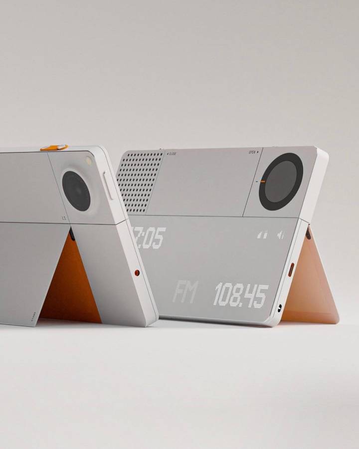 Two grey handheld devices standing on orange fold out stands, one showing a camera lens and the other a dot matrix display reading FM 108.45.