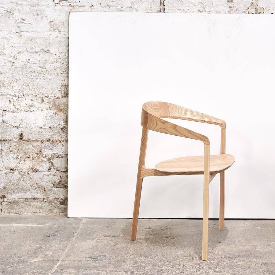 A pale timber chair with an arching back and arms standing on a concrete floor in front of a white board leaning on a painted brick wall.