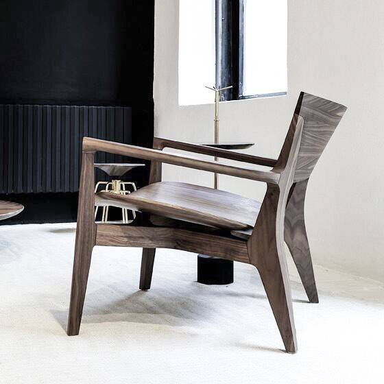 A walnut armchair with a tall tapered back, straight arm rails and a solid timber seat, in a room with a black wall and a slim brass side table.