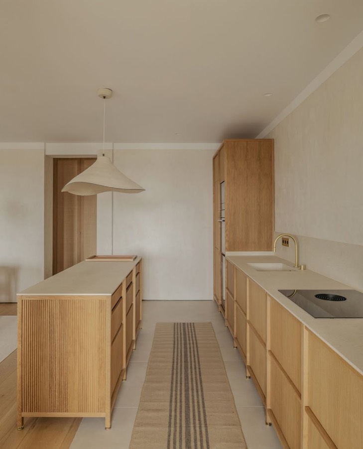 A pale oak kitchen with a long island, a striped floor runner and a pendant light.