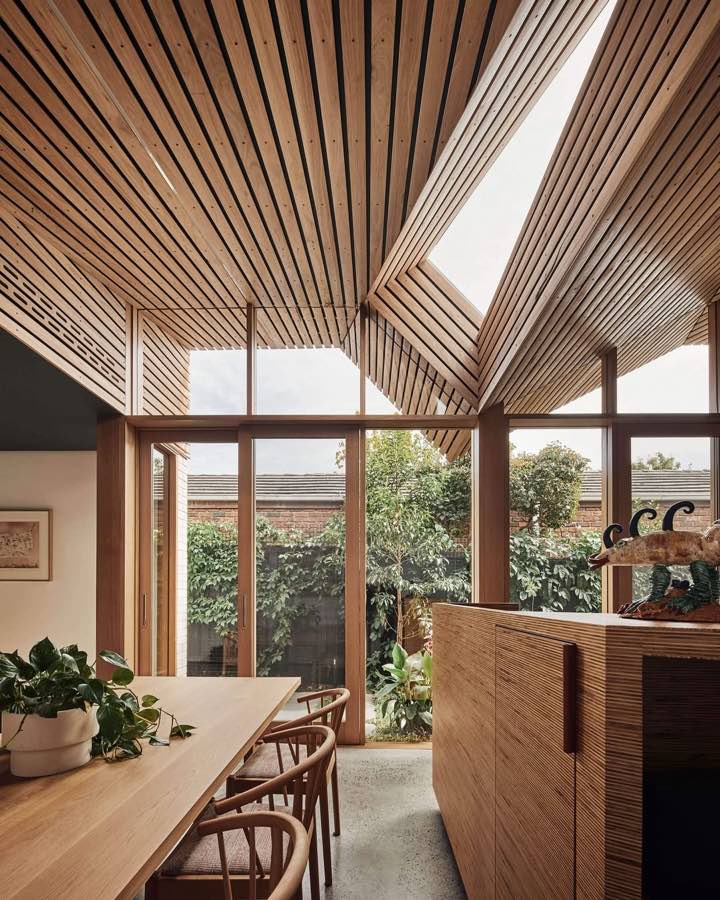 A dining room under a ceiling of angled timber battens with a skylight, and glass doors to a garden.