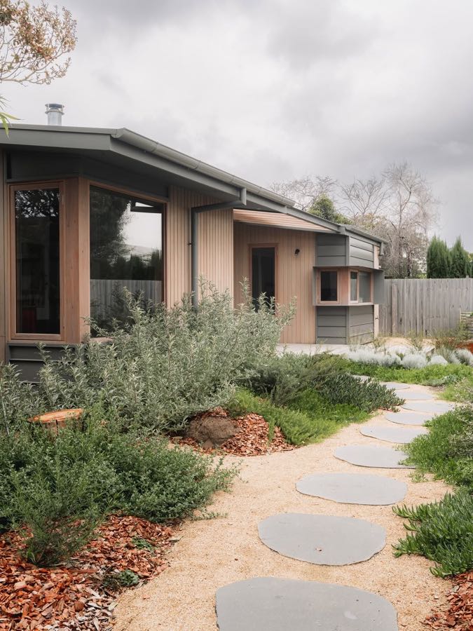 A single-storey house with a low angled roof behind a native garden with a stepping stone path.