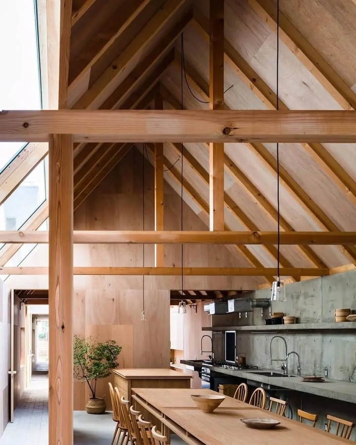 A room with an exposed softwood roof frame rising to a ridge, above a long table and a concrete kitchen bench.
