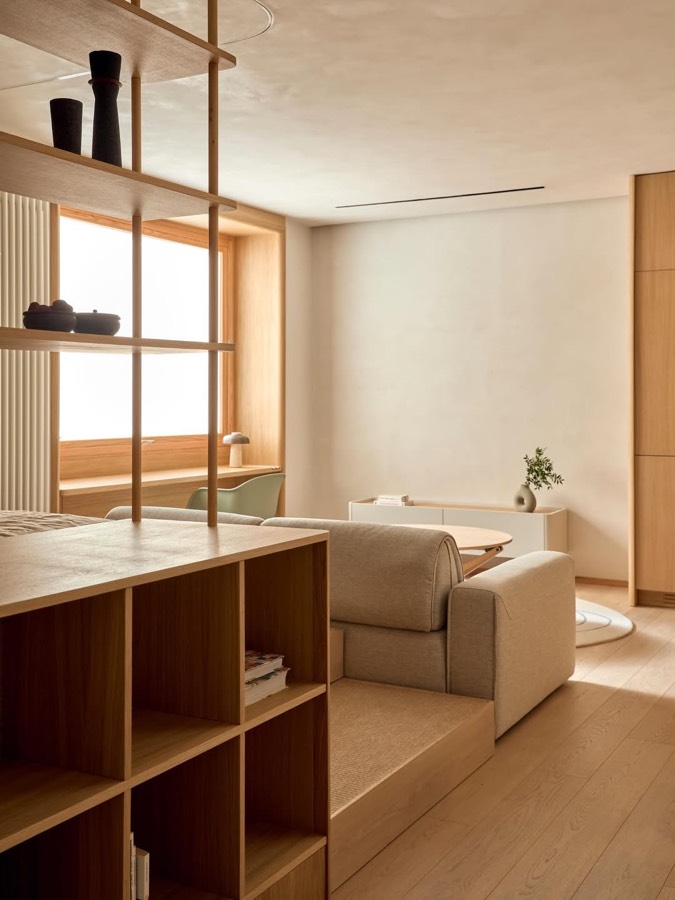 A living room with a low platform, a pale sofa and joinery fronted in translucent paper panels.