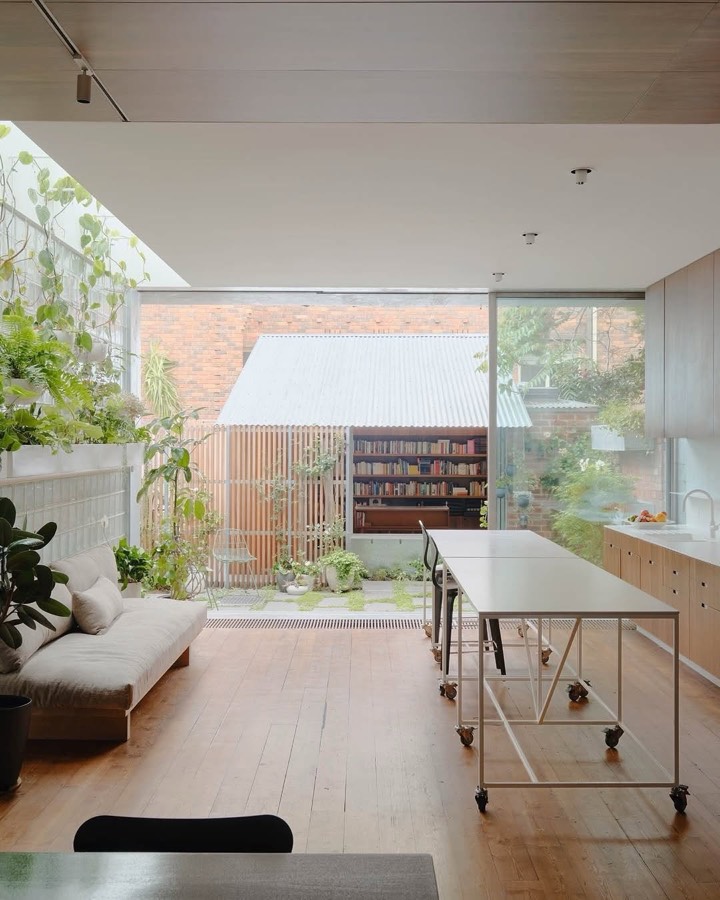 An open ground floor room with a steel trolley bench, looking out through full height glass to a garden studio.