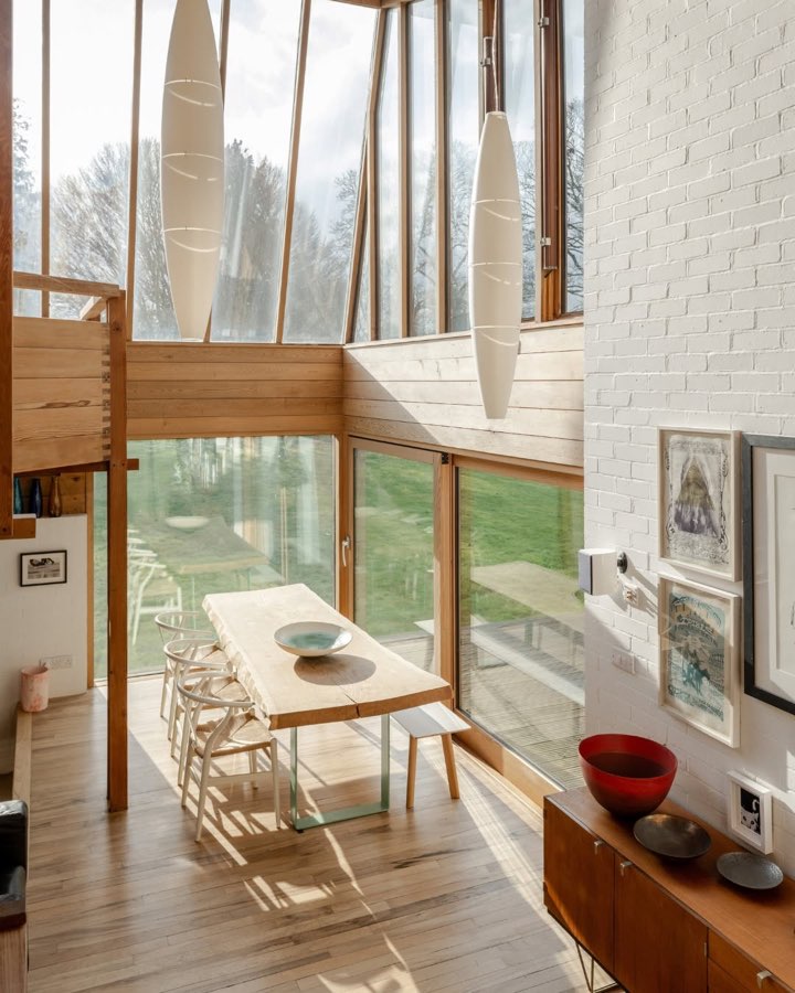 A dining table beside full height windows under tall paper pendant lights, with a white brick wall alongside.