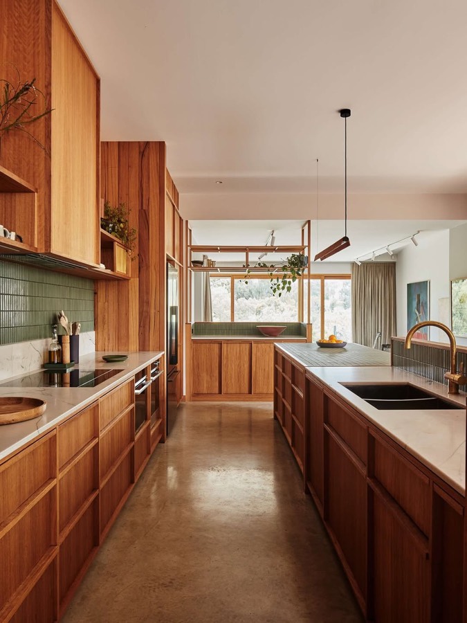 A long kitchen with timber cabinets, a green tiled splashback and a window seat at the far end.