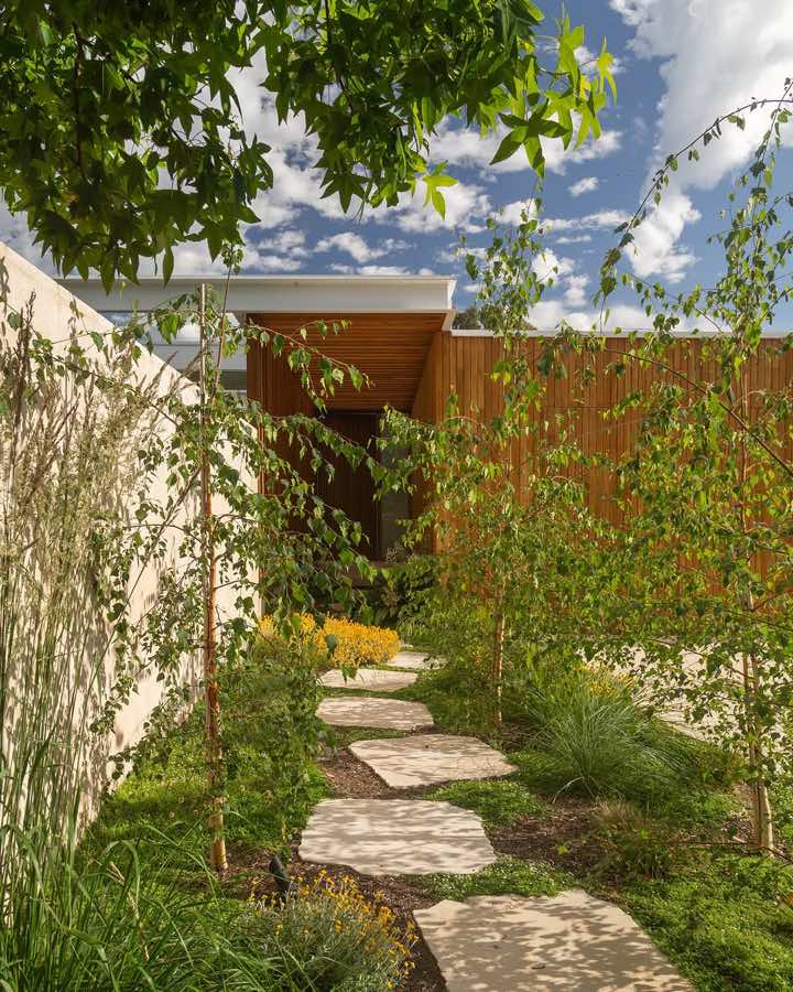 A stepping stone path through loose planting, running beside a bagged brick wall towards a timber fence.