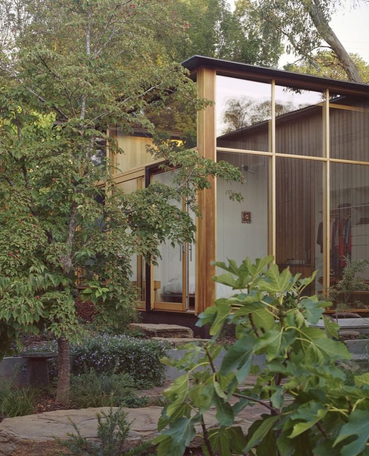 A timber and glass house standing among trees, with tall glazing set between slender frames.