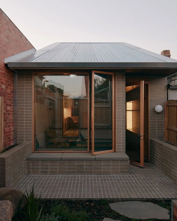 A brick rear addition with a low metal roof and timber framed glass doors opening to a paved yard.