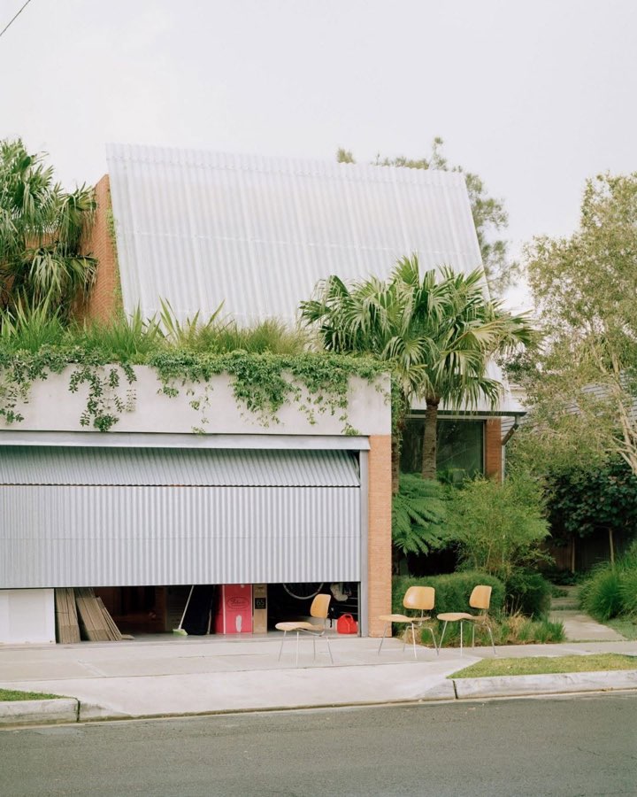 A brick house on a street corner with plants spilling over the garage roof and a translucent screen above.