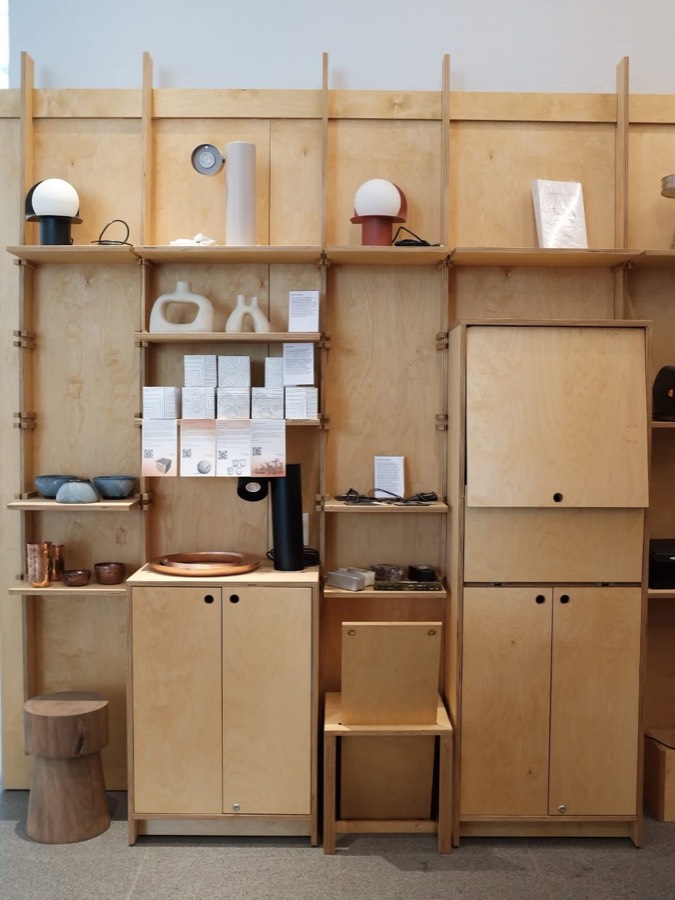 A freestanding plywood shelving and cabinet system holding books, ceramics and small objects.