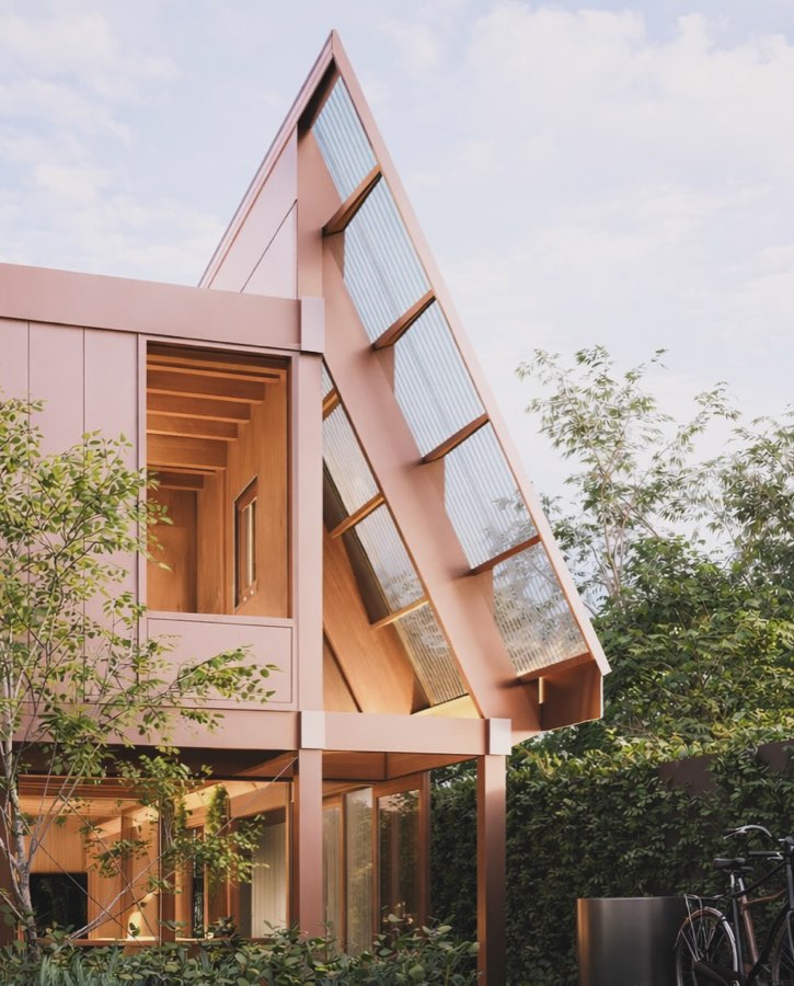 A render of a copper coloured two-storey addition with a steeply raked glazed roof above a garden.