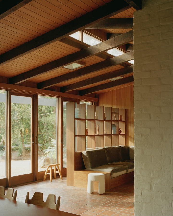 A living room with exposed dark beams, a brick floor and built-in shelving beside a low green sofa.