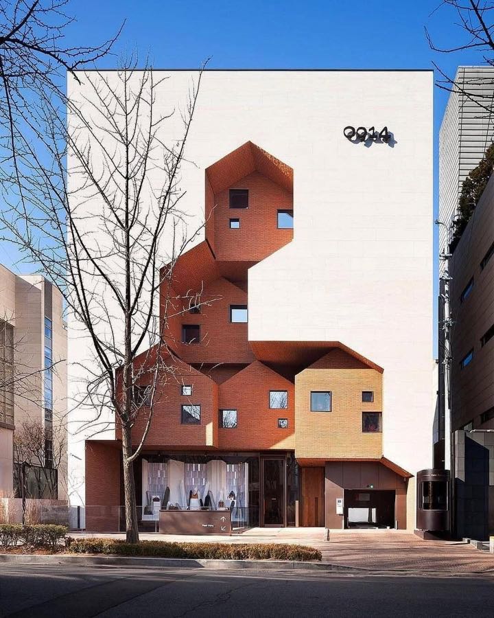 A brick building of stacked angled volumes with small square windows, on a city street.