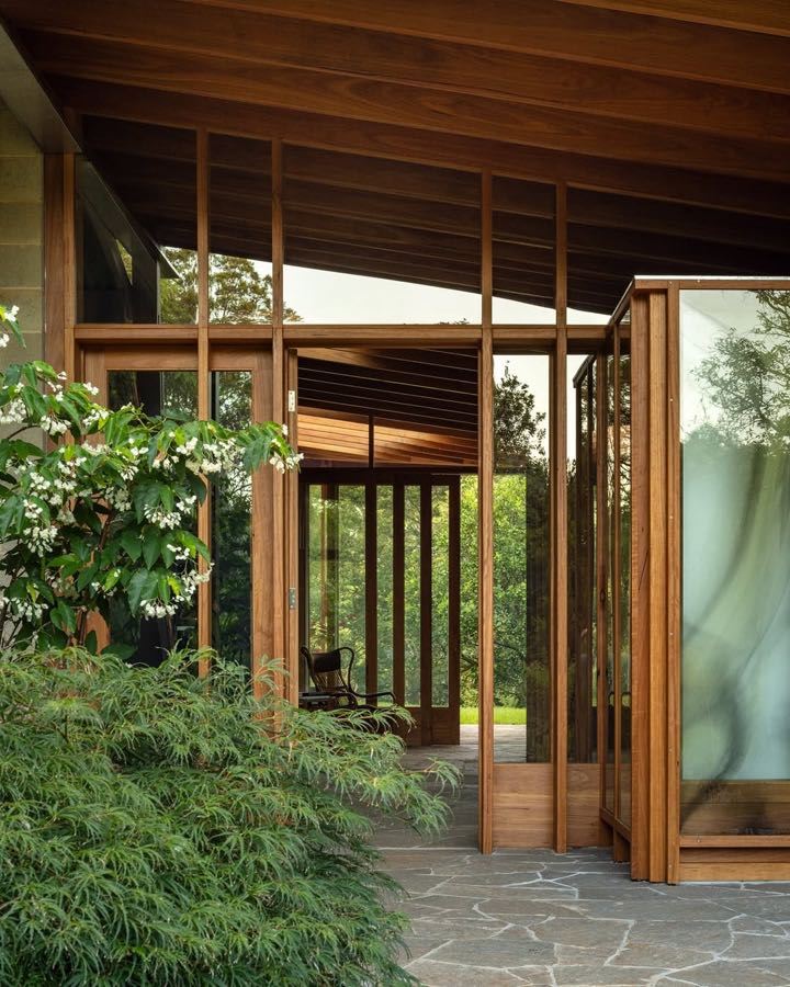 Timber posts and glass doors opening onto crazy paving, with heavy planting on both sides.