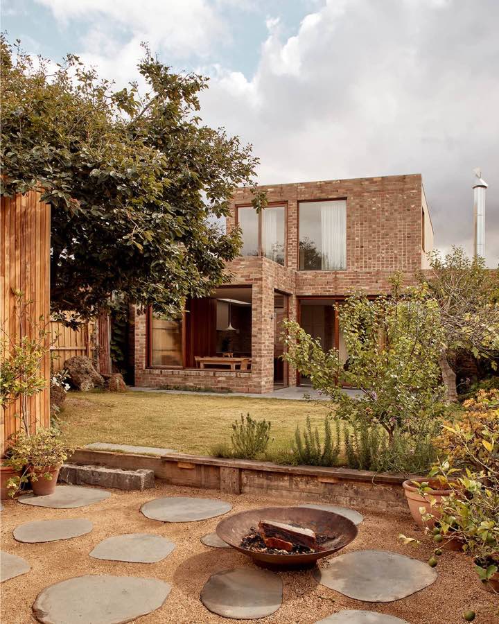 A brick house seen from its garden, with a fire pit on stepping stones and a lawn between.